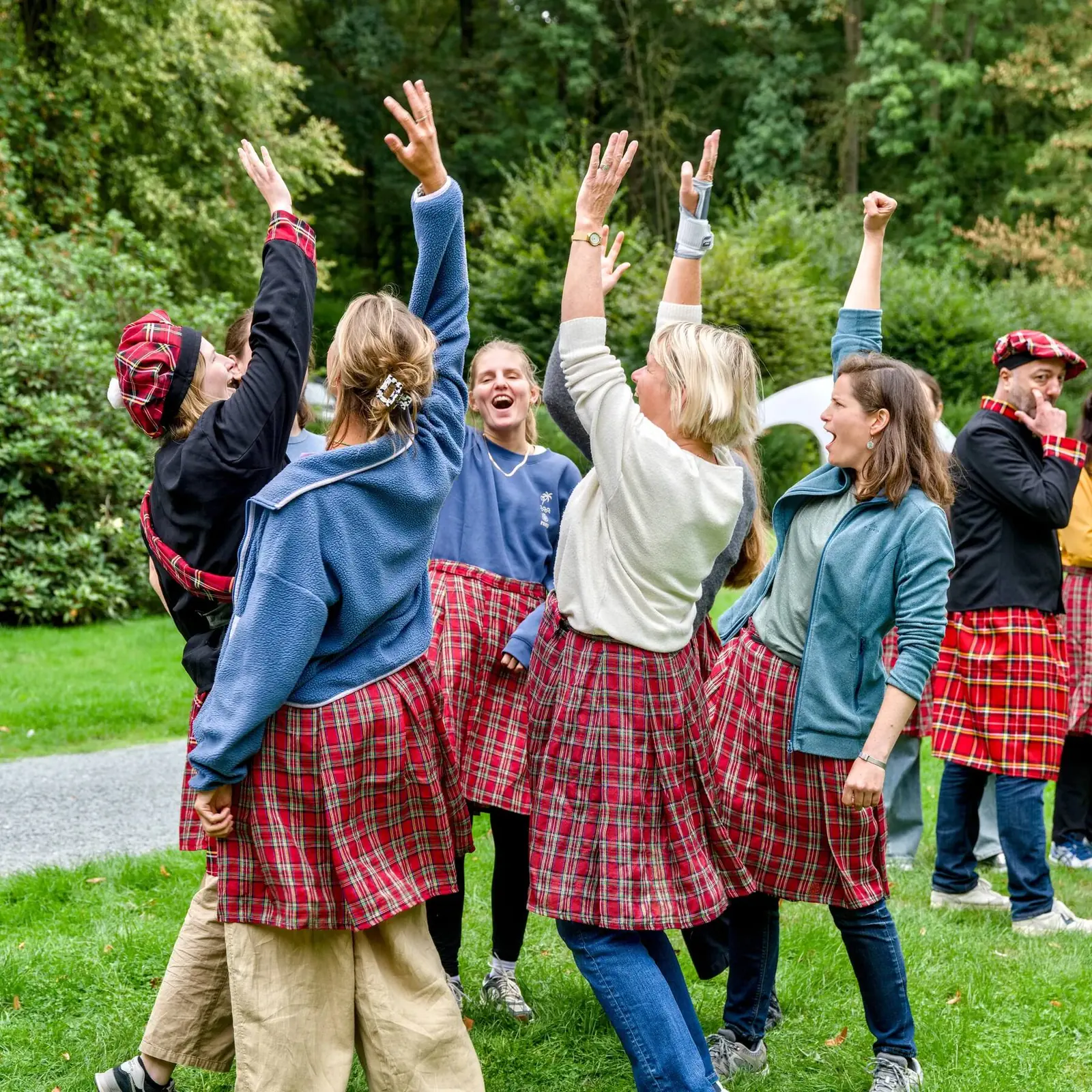 A kilted clan raises their arms and shouts in the park