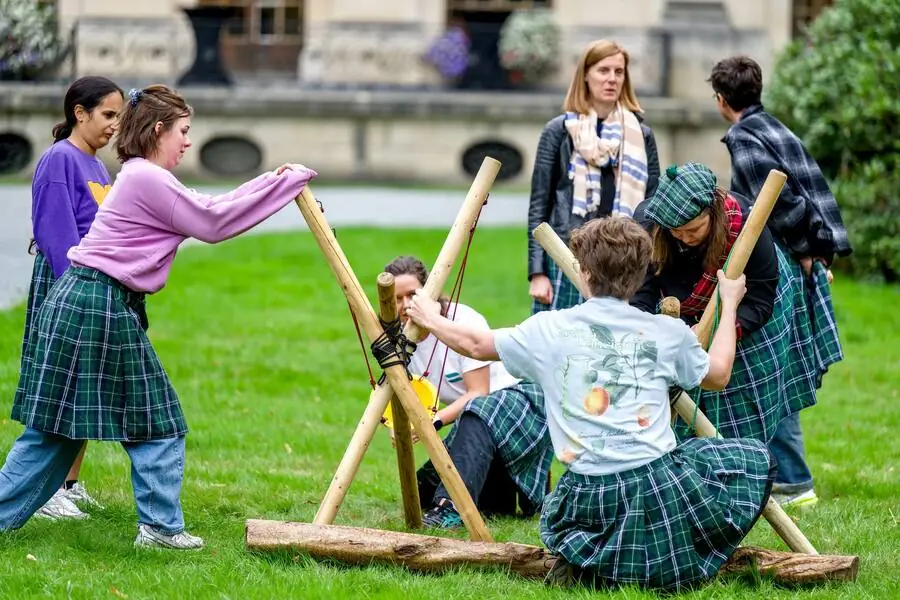 A kilted team lifts a wooden structure on the lawn