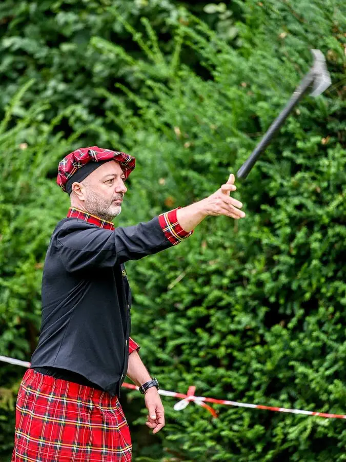 A participant in a kilt throws an axe at a wooden target
