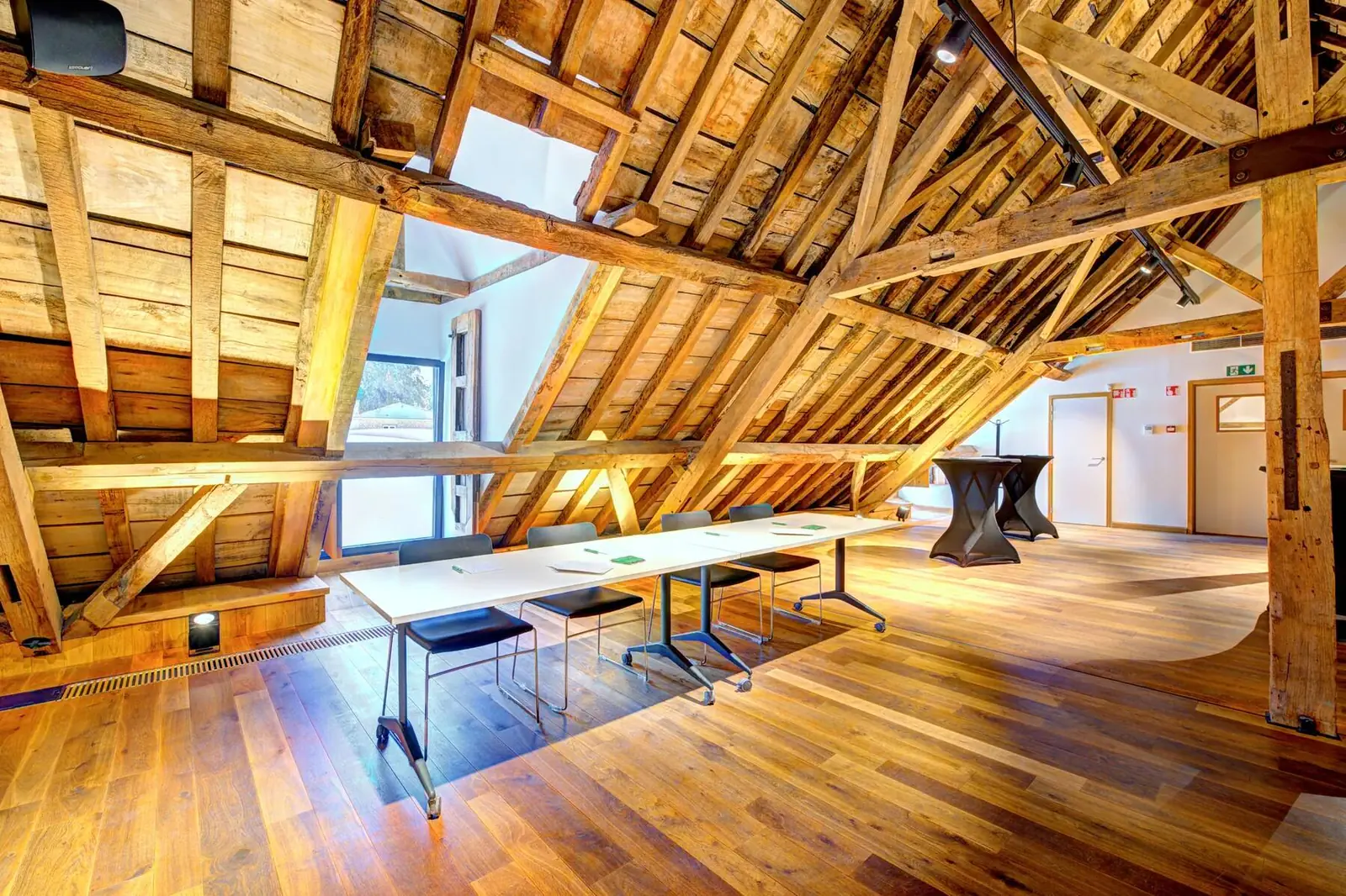 Large hall beneath exposed roof beams, work tables and high tables