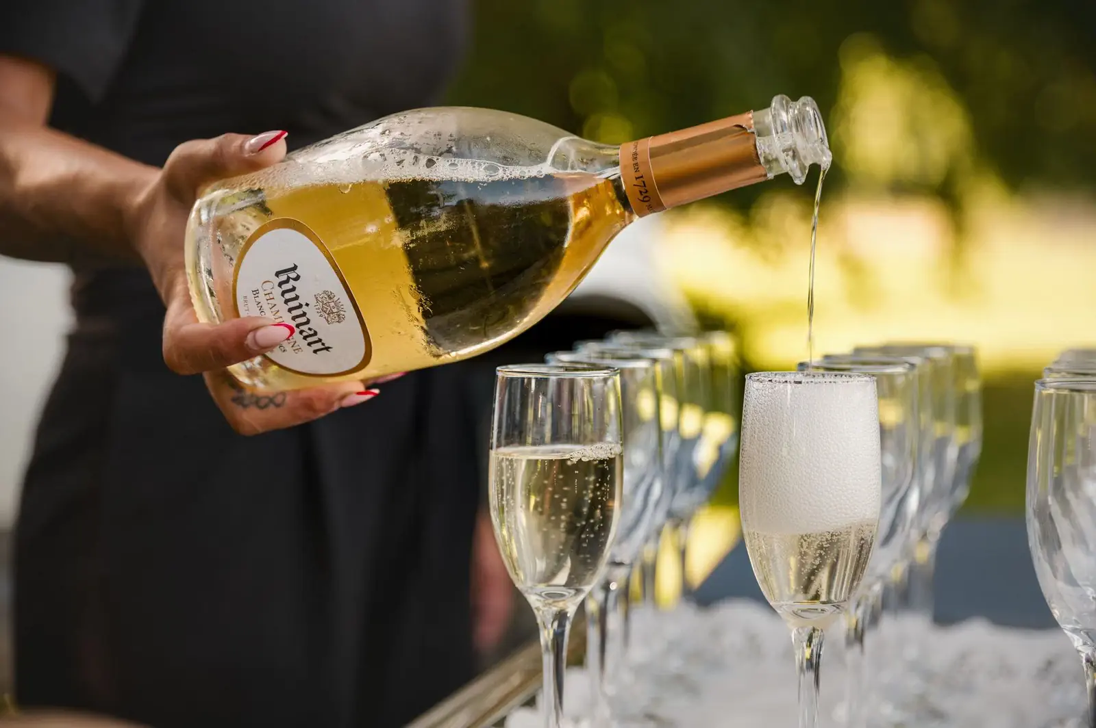 A waitress pours Ruinart champagne into a row of coupes