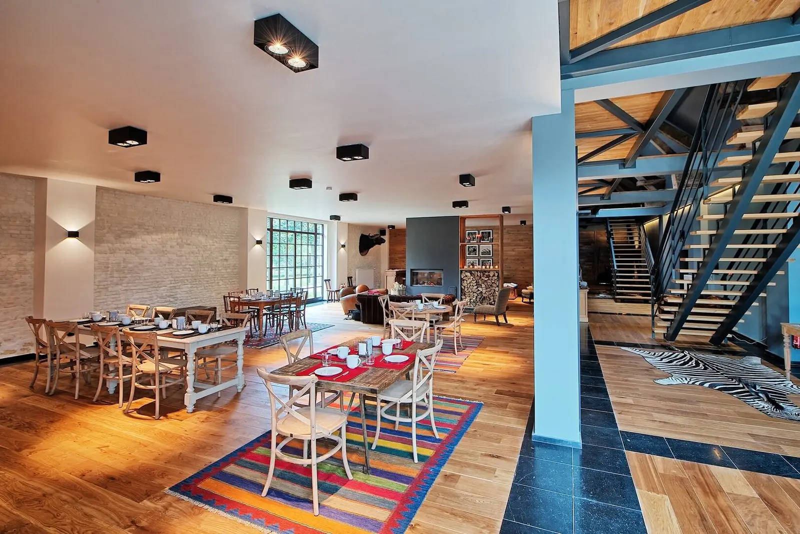 Dining room with colourful rugs, laid tables and a metal staircase